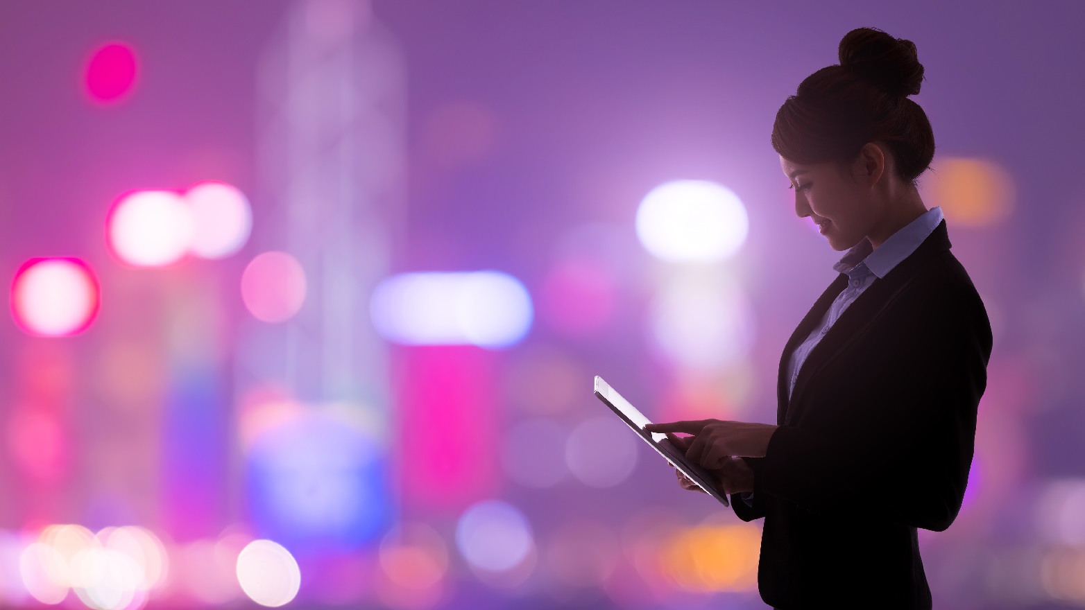 Woman using a tablet in front of a lit city scape at night